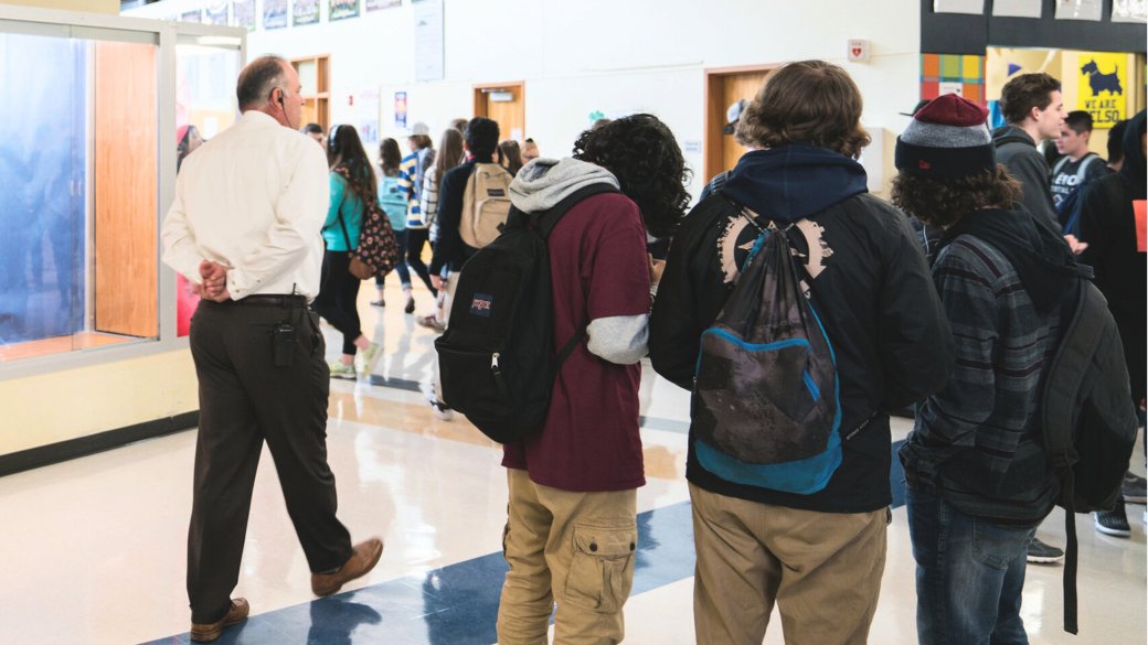 Students gather in a school hallway as an adult walks by.