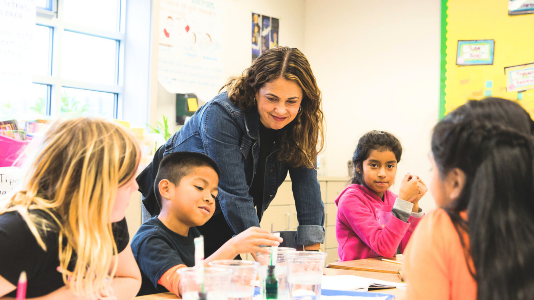 Teacher leans over to assist students with a science experiment in class.