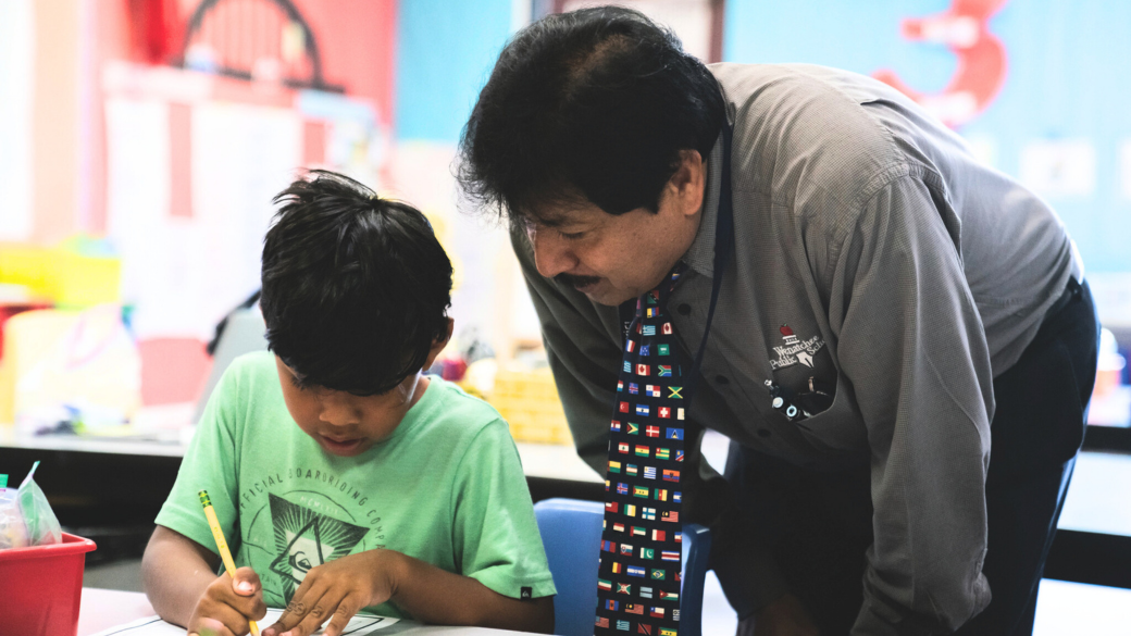 Teacher leans over to help a student with classwork.