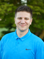 Smiling man in a bright blue Nike polo shirt, standing outdoors with a blurred green background.