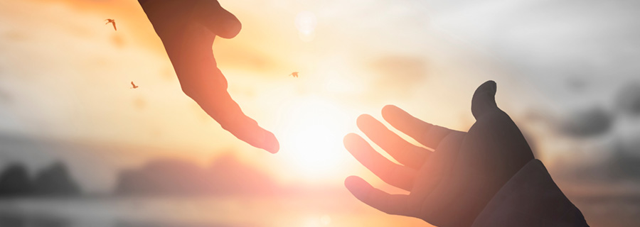 photo of two hands trying to reach each other against a beach background with the sun setting