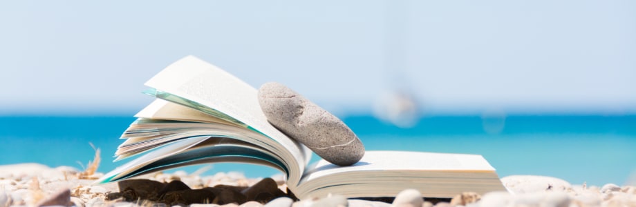 open book on a beach with a rock holding open the pages
