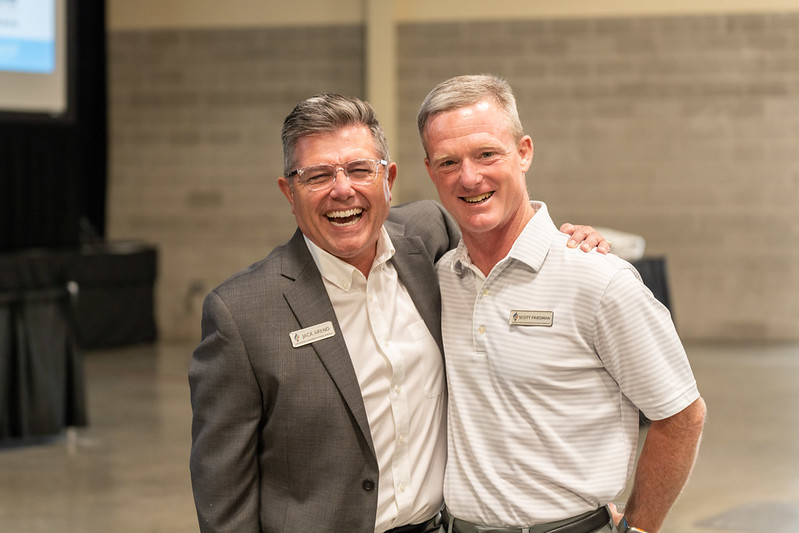 Two men in dress clothes half hugging and laughing histerrically.