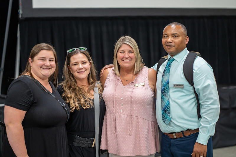 Three white women and one black man in business casual dress posing together