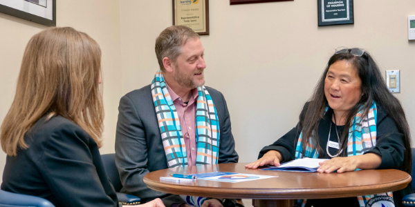 AWSP members wearing matching scarves meet with a legislator at a round table, discussing documents during an advocacy meeting.