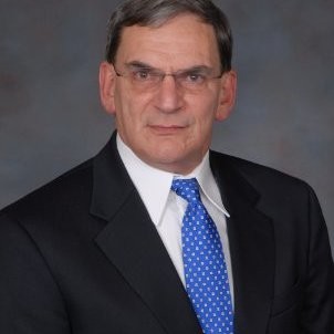 A headshot of a middle-aged man in glasses wearing a suit.