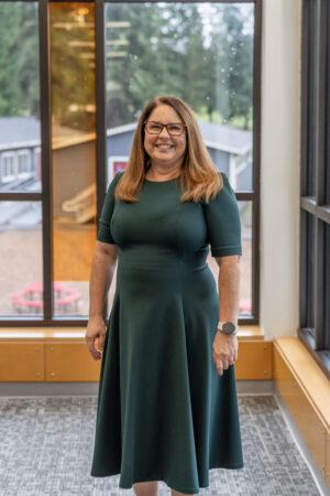 90c319e4 0eeb 40c2 9070 2c7fbad3e087hair and glasses wearing a green dress in front of a window in her school. 