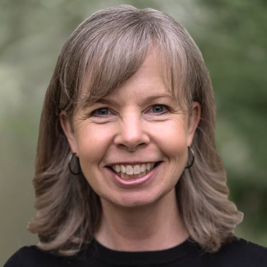 A smiling white woman with shoulder length brown and gray hair in a black shirt.
