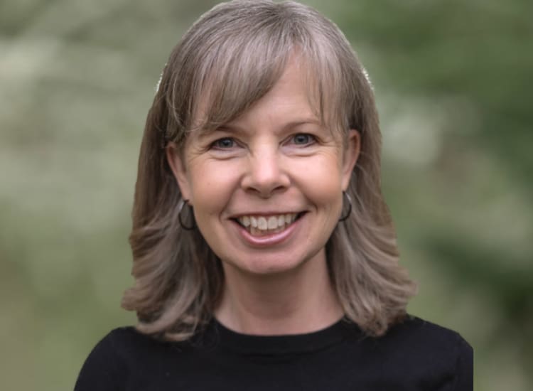 A smiling white woman with shoulder length brown and gray hair in a black shirt.