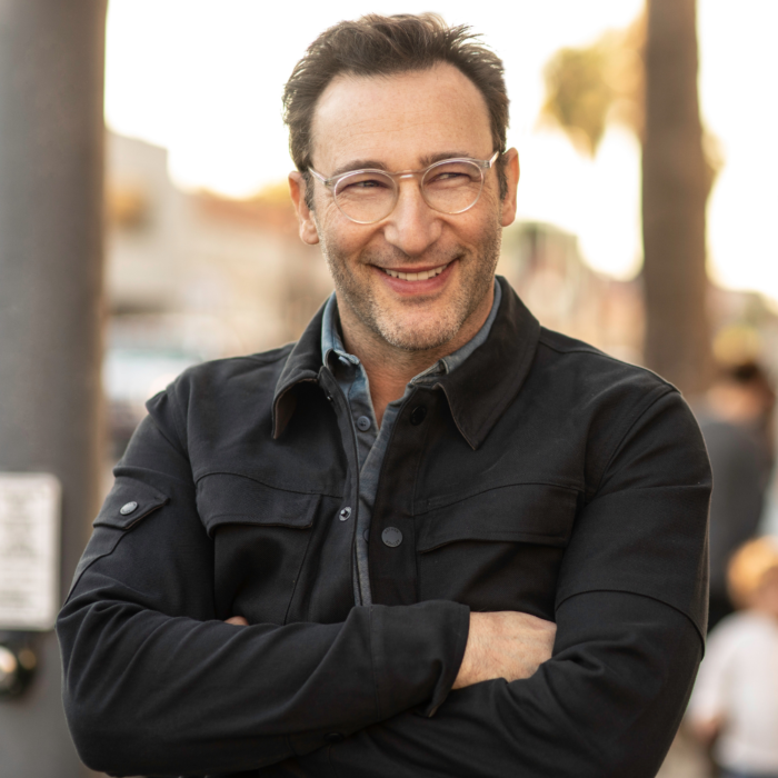 Smiling man with glasses and short dark hair, standing outdoors with his arms crossed and wearing a dark jacket over a collared shirt.