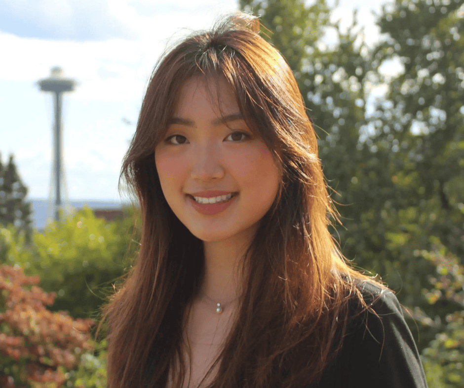 Smiling woman with long hair outdoors, with trees and Seattle’s Space Needle in the background.