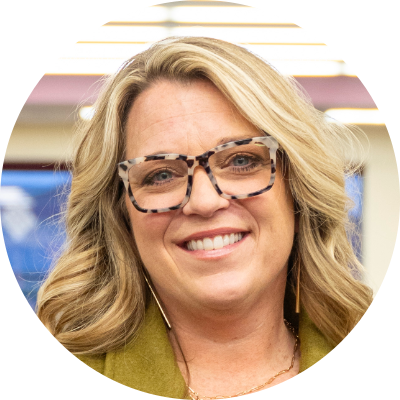 PODCAST | Kim Doepker & Heidi Fagerness on Leadership, Learning, and Finding Your People Smiling woman with shoulder-length blonde hair and tortoiseshell glasses, wearing a green jacket and long earrings.